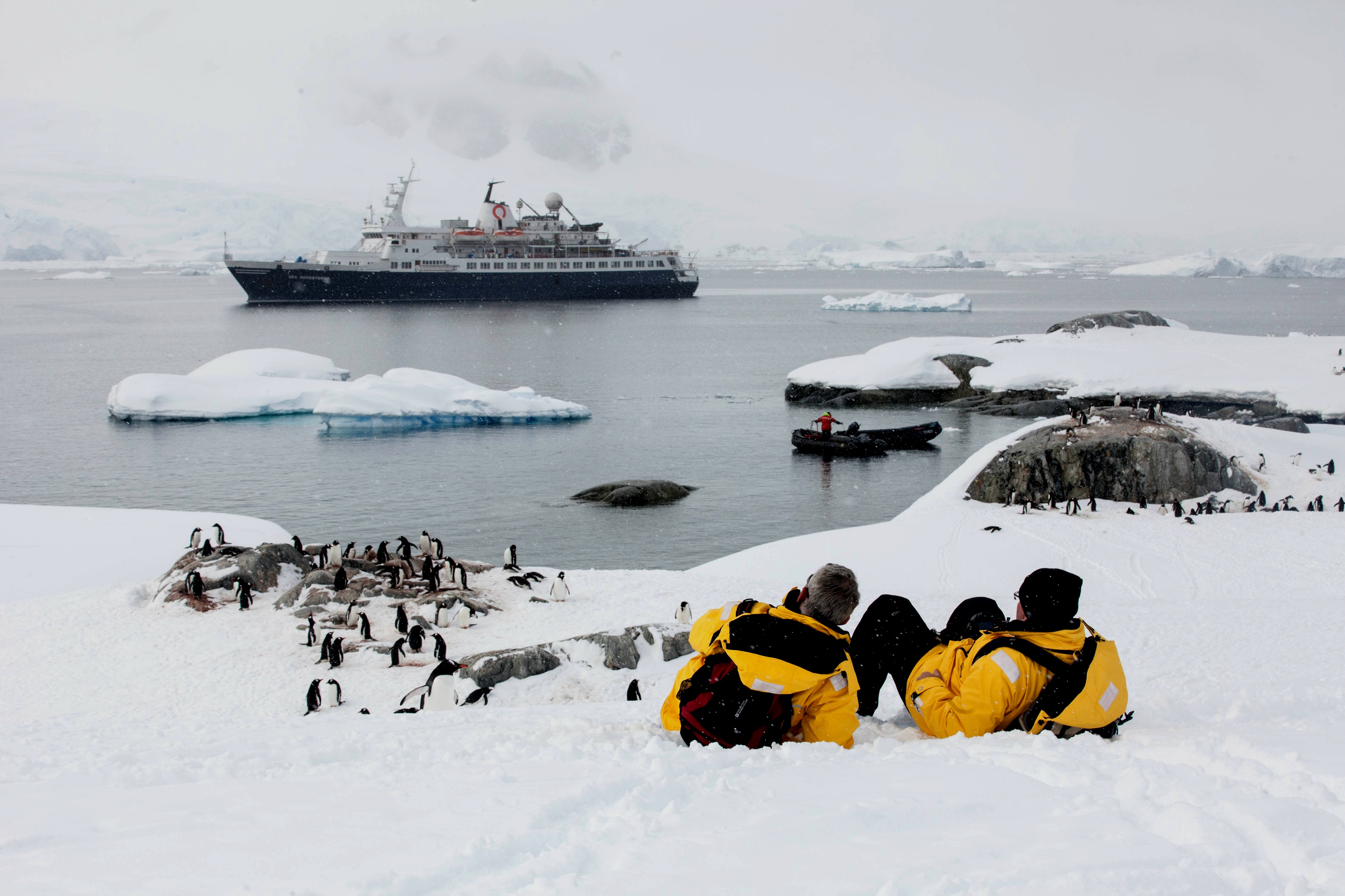 Quark passengers relax and enjoy the view of a penguin colony against a backdrop of frigid Antarctic water.